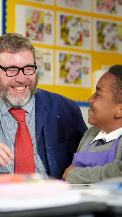Teacher smiling and talking with a pupil in an art classroom.