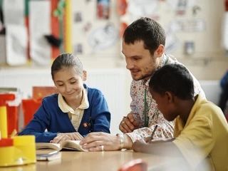 Primary teacher sat alongside two students while helping them with their work