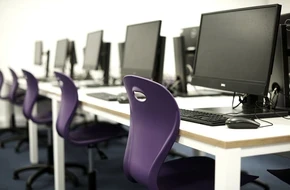 Row of computer workstations with purple chairs in a modern classroom or computer lab.