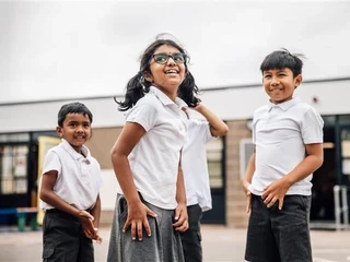 Three primary school children smiling and playing outside a school building