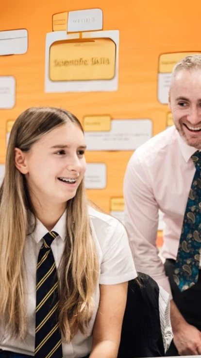 Teacher supporting two secondary school pupils during a classroom activity.